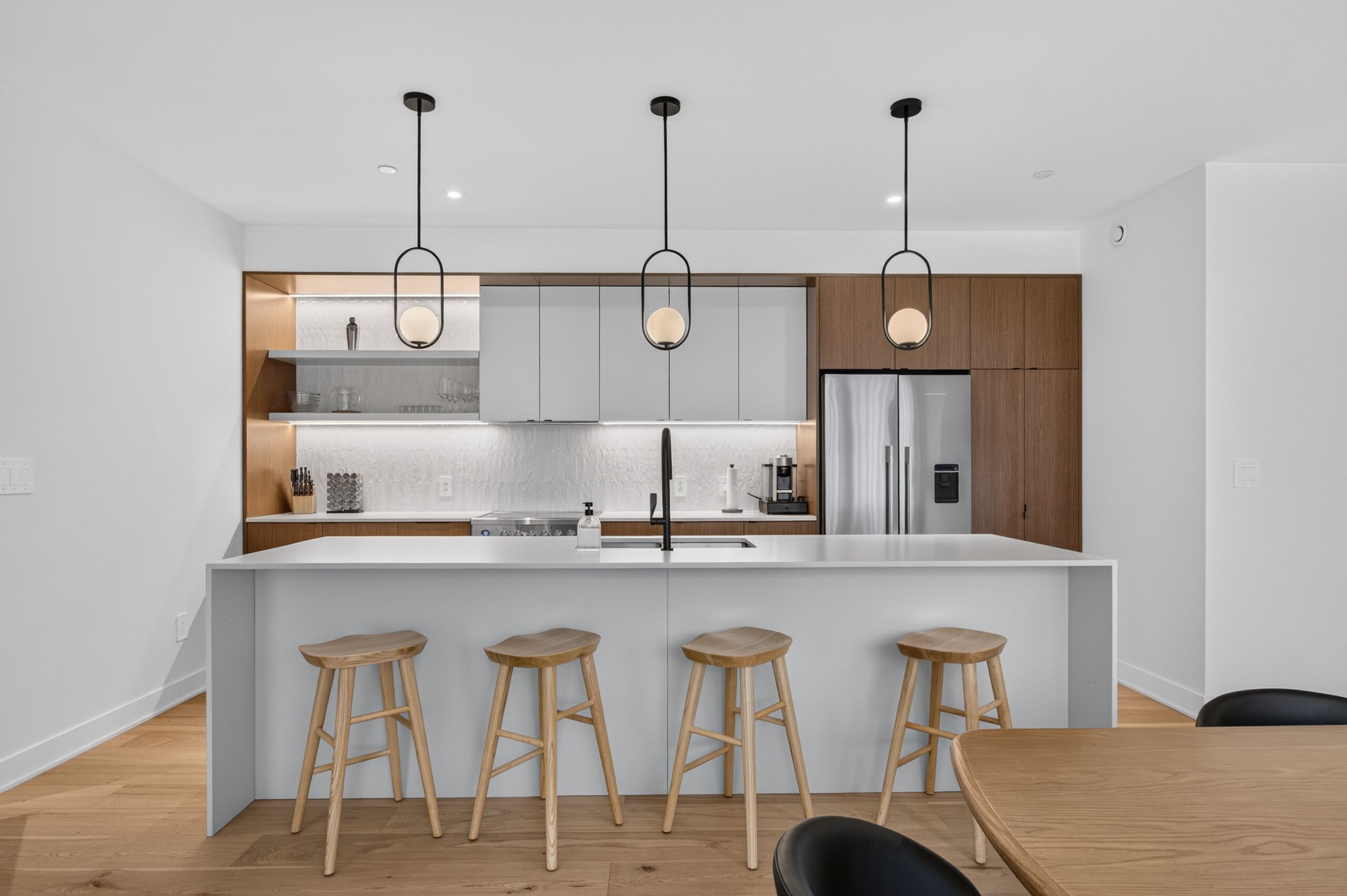 Una cucina moderna con isola centrale, sgabelli da bar e luci a sospensione.
