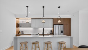 A modern kitchen with a central island, bar stools, and pendant lighting.