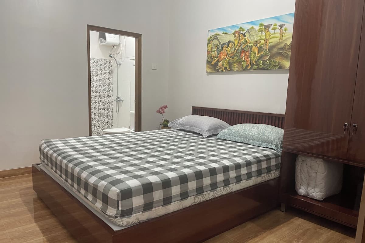A bedroom with a checkered bedspread, a wooden headboard, a wooden wardrobe, and a painting on the wall.