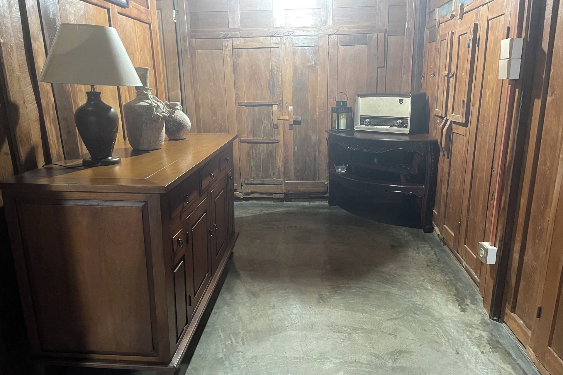 A wooden hallway with a vintage radio, a lamp, and a decorative vase on a wooden cabinet.