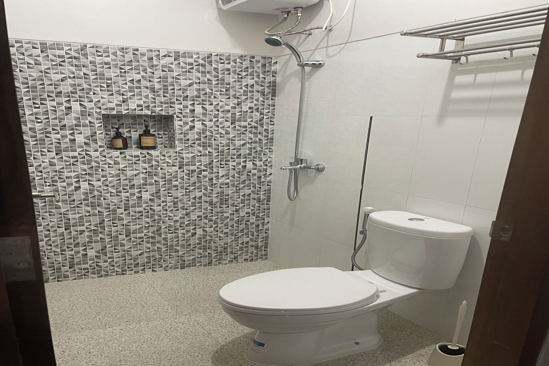 A bathroom with a white toilet, a shower with a handheld showerhead, and a tiled wall with a geometric pattern.