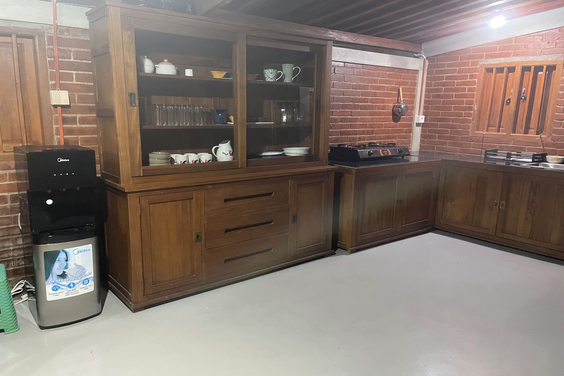 A kitchen with wooden cabinets, a water dispenser, and a brick wall.