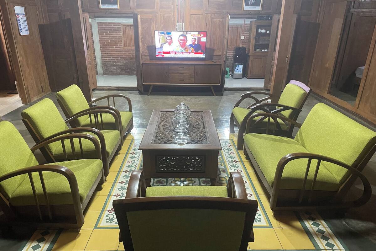 A room with a wooden cabinet, a television, and green upholstered chairs arranged around a central coffee table.