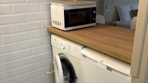 A compact laundry room with a washing machine and a microwave on a wooden countertop. - Horizon Caraibes (Le Gosier)