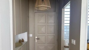 A hallway with a beige door, a hanging light fixture, and a tiled floor. - Horizon Caraibes (Le Gosier)