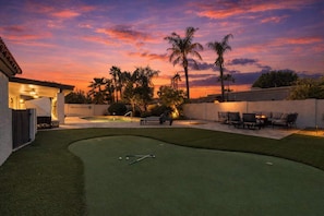 Een achtertuin met een putting green, buitenzitplaatsen en palmbomen.