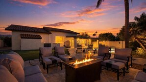 A patio with outdoor furniture and a fire pit, surrounded by a house with a tiled roof and a well-maintained lawn.