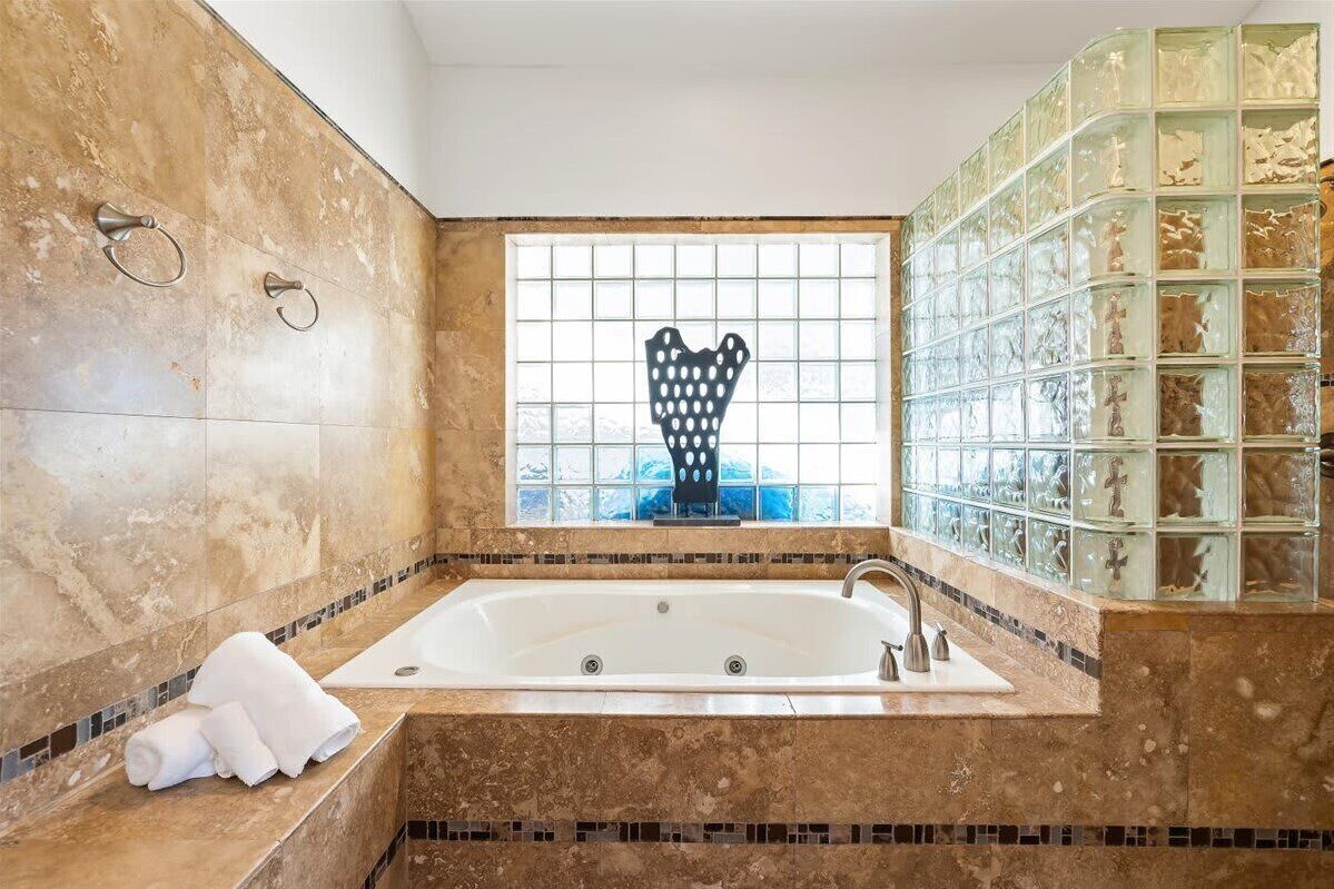 Ein Badezimmer mit einer großen Badewanne, einem Fenster mit dekorativem Ausblick und einer mit Mosaikbordüre versehenen Fliesenwand.