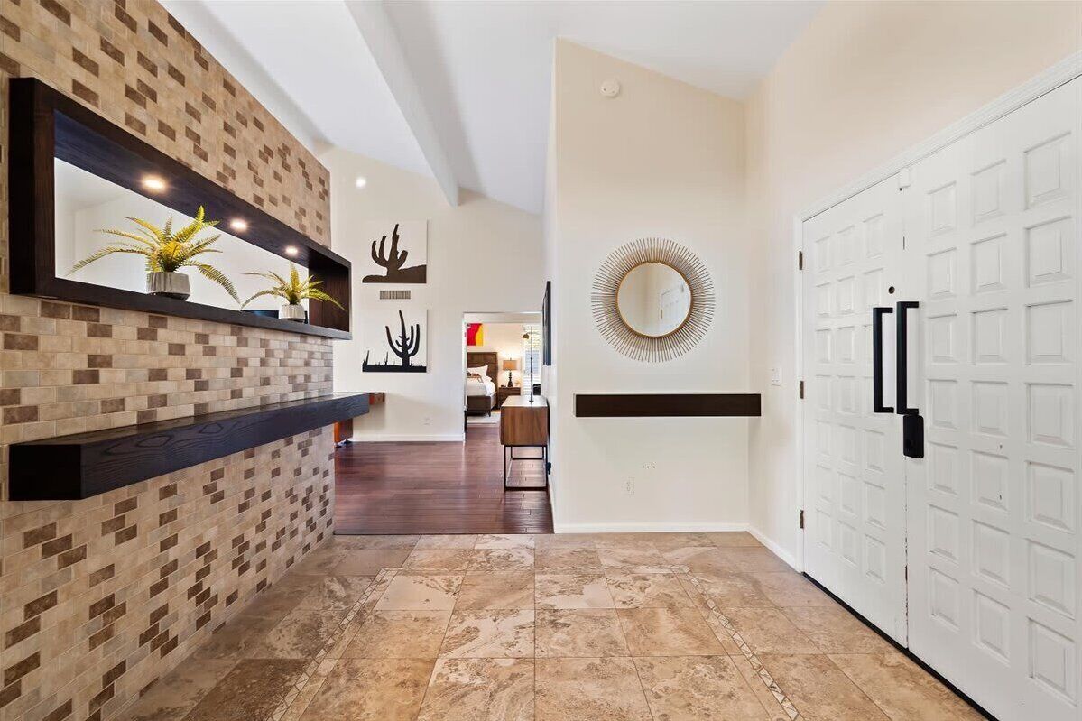 A hallway with a tiled floor, a wall-mounted shelf with plants, a mirror, and a white door.