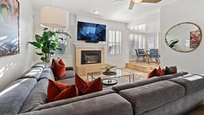 A modern living room with a sofa, TV, fireplace, and dining area.