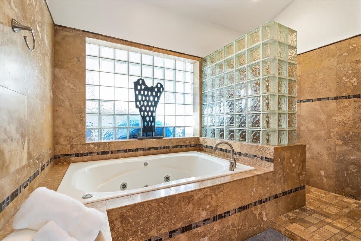 Een badkamer met een groot bad, een raam met een decoratie in de vorm van een hart, en mozaïek wandtegels.