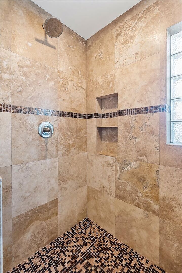 A shower with beige tiles, a tiled floor, and a small shelf.