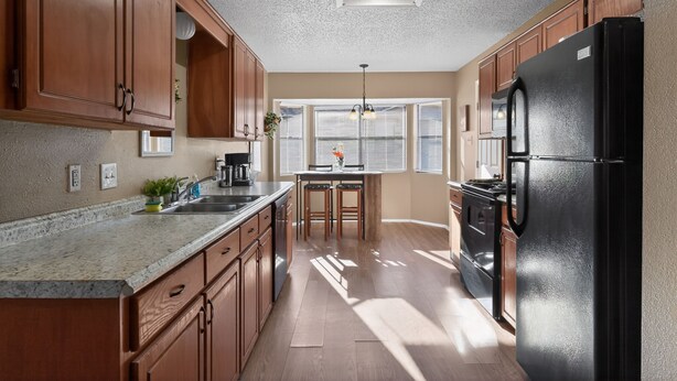 A kitchen with wooden cabinets, a black refrigerator, a granite countertop, and a window with blinds. -  3BR Home Near Fort Cavazos Game Room Military Friendly (Killeen)
