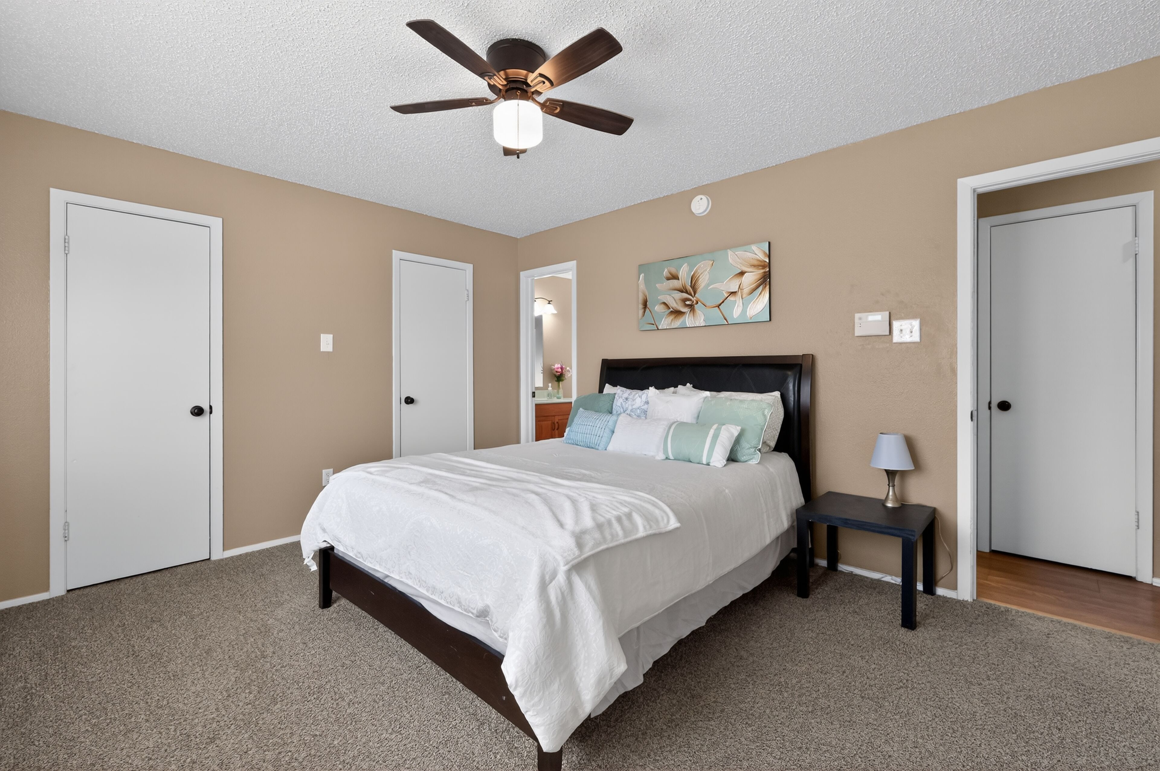 A bedroom with a bed, a nightstand, a ceiling fan, and two doors.