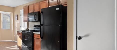 Una cocina con armarios de madera, un refrigerador negro, una estufa y un microondas.