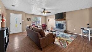 A living room with a brown leather sofa, a coffee table, a patterned rug, a fireplace, and a ceiling fan. -  3BR Home Near Fort Cavazos Game Room Military Friendly (Killeen)
