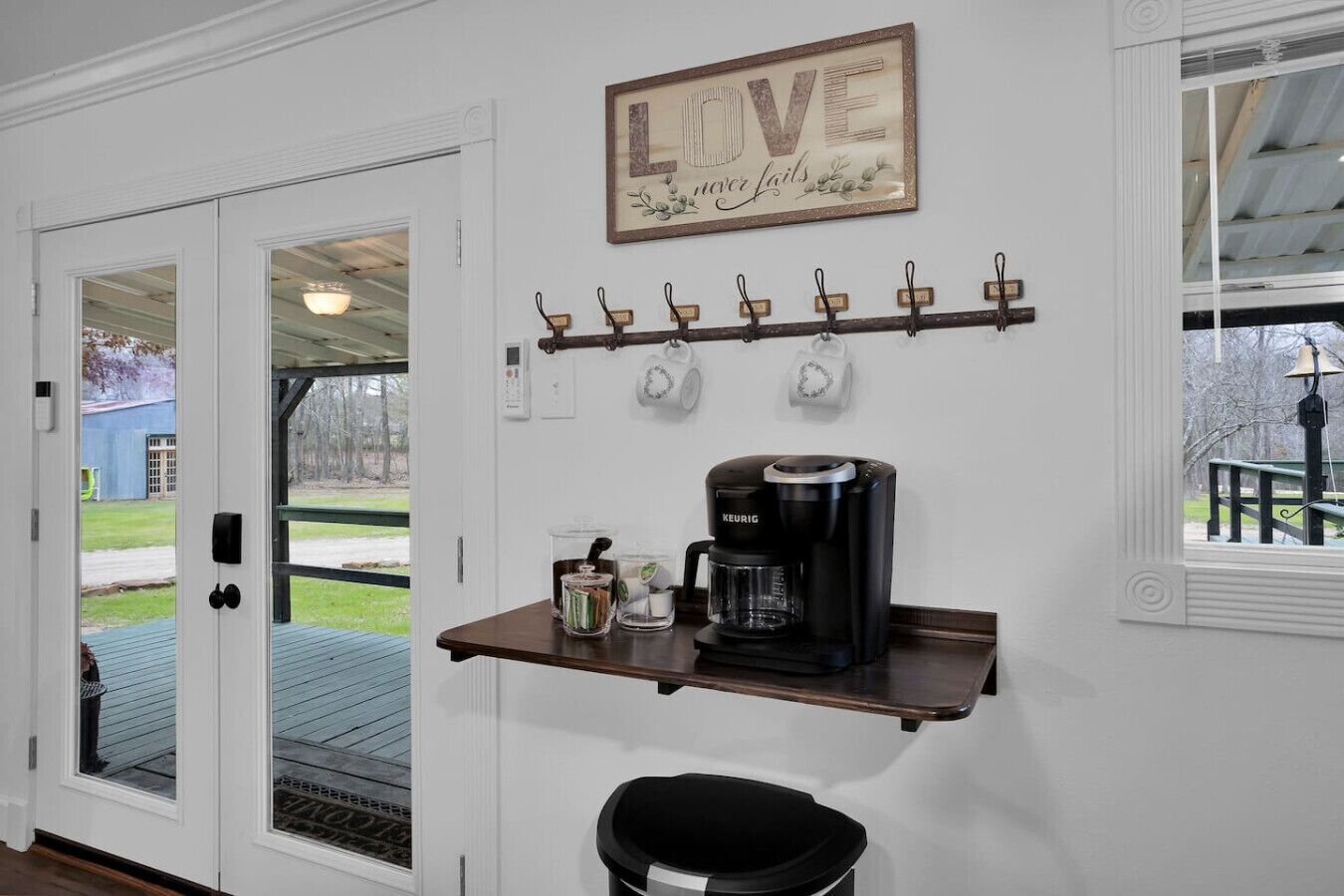 A kitchen area with a coffee maker, a shelf with mugs, and a 'LOVE never fails' sign.
