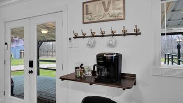 A kitchen area with a coffee maker, a shelf with mugs, and a 'LOVE never fails' sign.