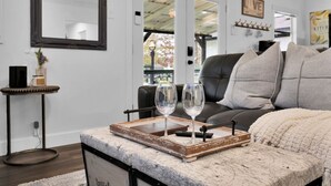 A modern living room with a leather sofa, a coffee table with a tray holding two wine glasses, and a large mirror on the wall. - Peaceful Romantic Cottage with Fire Pit and Pond Near Lake Conroe (Montgomery)