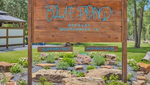 A wooden sign with 'Blue Pond Retreat Montonomy, TX' and 'Bluebonnet Belle' and 'Wildflower Willow' labels. - Peaceful Romantic Cottage with Fire Pit and Pond Near Lake Conroe (Montgomery)