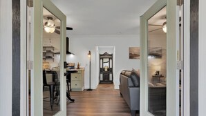 A hallway with a kitchen area on the left, a dining area with a table and chairs, and a living room with a sofa and a TV on the right. - Peaceful Romantic Cottage with Fire Pit and Pond Near Lake Conroe (Montgomery)