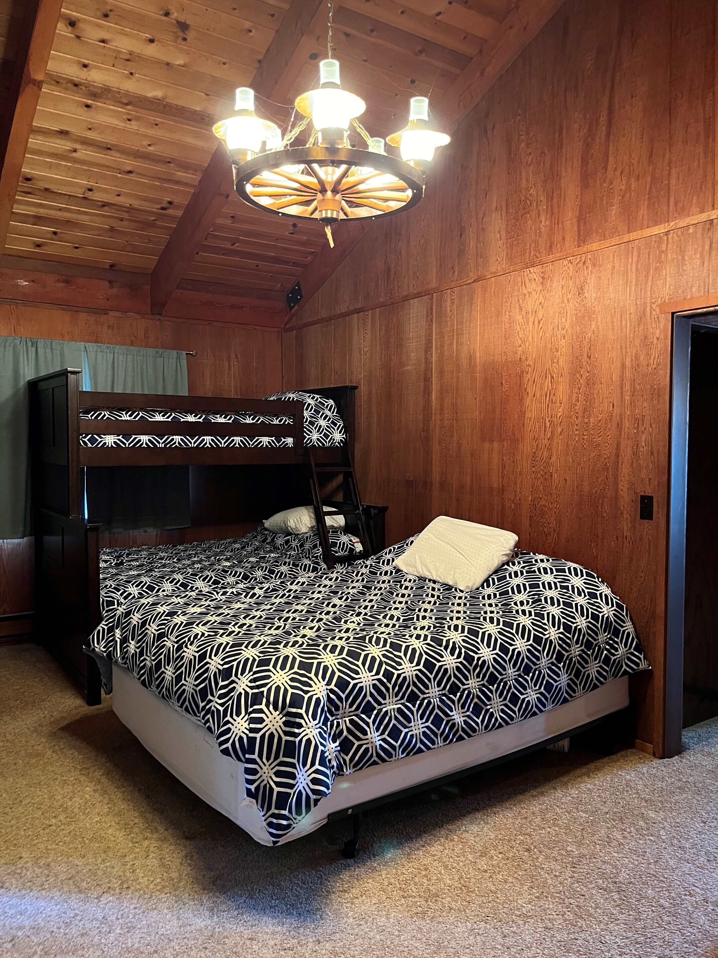 A bunk bed with a geometric patterned bedspread, a wooden ceiling, and a chandelier.