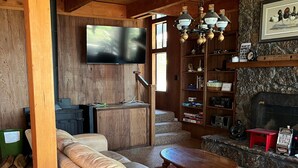 Un salon chaleureux avec un canapé en cuir, une table basse, une cheminée et un téléviseur fixé au mur.