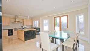 A modern kitchen with a central island, a dining area with a glass table, and large windows providing natural light. - 6000 sqft Executive 6 BR Home in Prestigious Area (Mississauga)