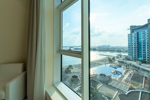 A view from a hotel room window overlooking a beach resort area with a pool, palm trees, and a large building. - Stunning 3BR at the Palm w/ Beach Access (Dubai)