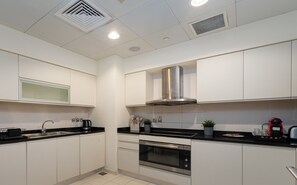 A modern kitchen with white cabinets, a stainless steel range hood, a built-in oven, and a black countertop.