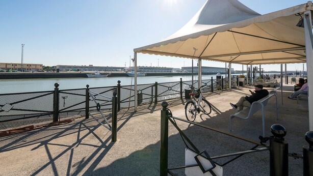 Terraza a la orilla del río con zona de estar cubierta, una bicicleta y vistas al agua.
