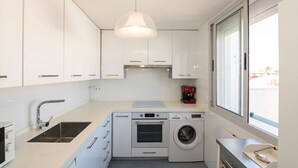 Una cocina moderna con armarios blancos, horno empotrado, lavadora y un amplio ventanal.