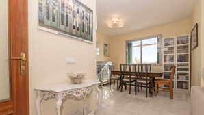 Un área de comedor con una mesa y sillas, una consola blanca, una cesta de mimbre y una ventana con persianas.