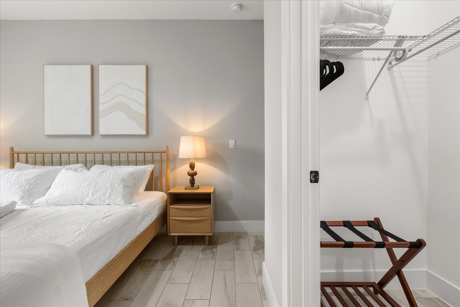 Un dormitorio con cama, mesita de noche, lámpara y dos obras de arte colgadas en la pared.