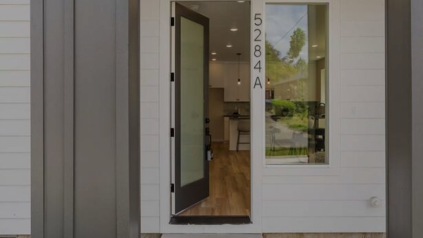 A modern house entrance with a glass door leading to a kitchen area.