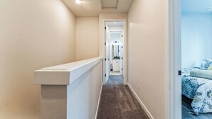 A narrow hallway with a white bench on the left, leading to a bedroom with a blue floral bedspread.