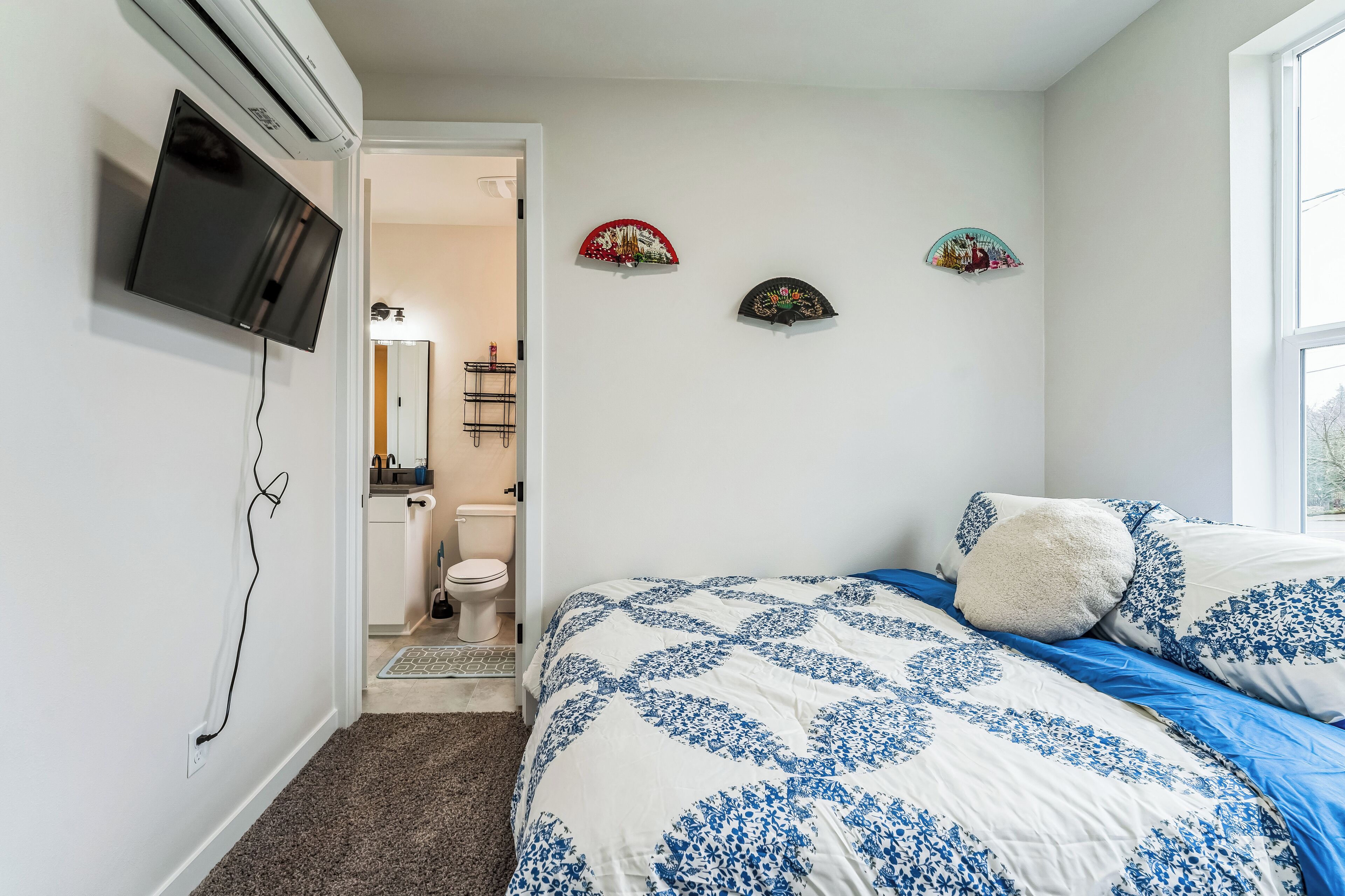 A bedroom with a bed, a TV mounted on the wall, and a door leading to a bathroom.
