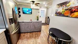 A compact kitchen with a built-in refrigerator, a grey sofa, and a dining area with metal chairs. - FREE NIGHT! TV In Bedroom, Patio, Private  (Houston)
