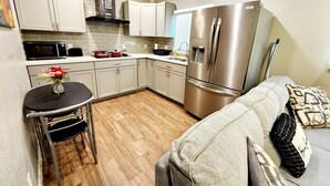 A compact kitchen with white cabinets, a stainless steel refrigerator, a microwave, and a small dining area with a table and chairs. - FREE NIGHT! TV In Bedroom, Patio, Private  (Houston)