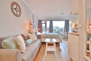 A modern bedroom with a large bed, a small table, a sofa, and a wall clock. - Haus Adria Apartment 28 Küstenliebe - Haus Adria (Scharbeutz)
