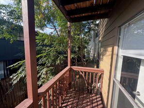 A wooden deck with a railing, surrounded by trees and a building. - Walkable Culdesac by Barton and Zilker (Austin)