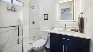 Ein modernes Badezimmer mit Glasdusche, Toilette, Waschtisch mit Spiegel und Handtuchhalter.