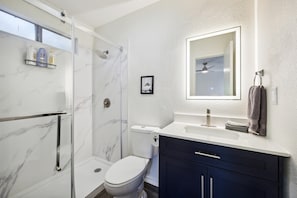 Un bagno moderno con box doccia in vetro, un water, un mobile lavabo con specchio e un porta asciugamani.