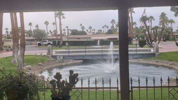 A covered outdoor area with a view of a fountain, palm trees, and a building in the background.