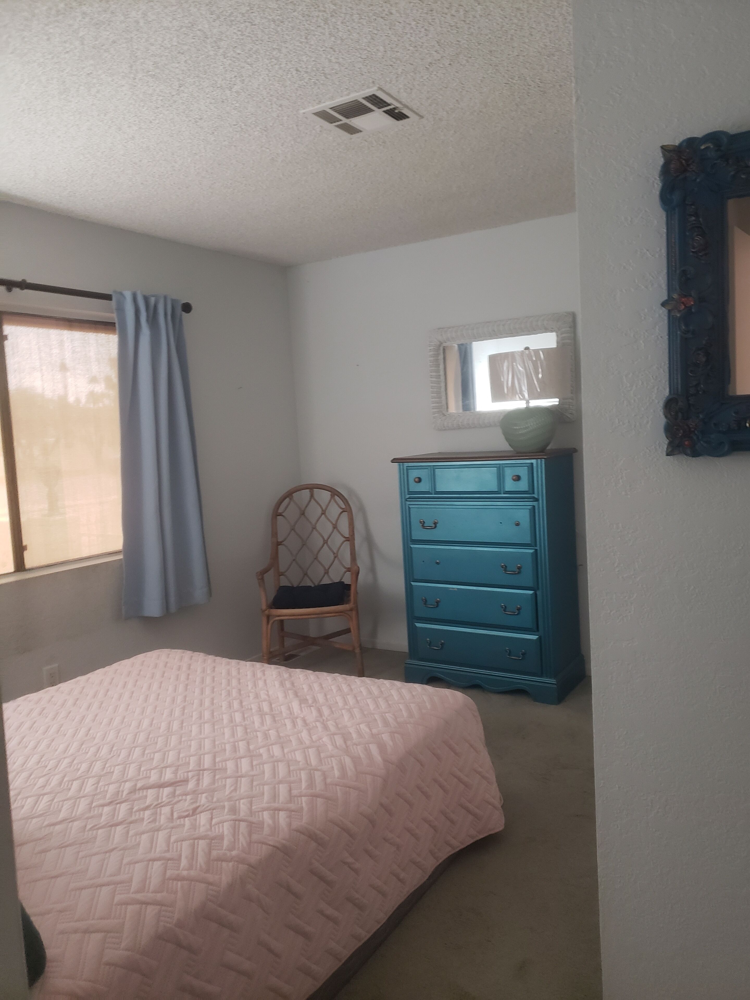 Ein Schlafzimmer mit Bett, Kommode, Stuhl und einem Fenster mit Vorhängen.
