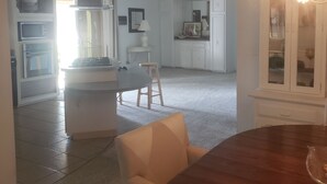 A spacious living area with a dining table, a kitchen in the background, and a staircase leading to another level.