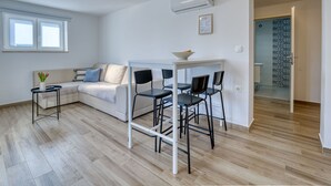 Una sala moderna con un sofá, una mesita redonda y una zona de comedor con sillas.