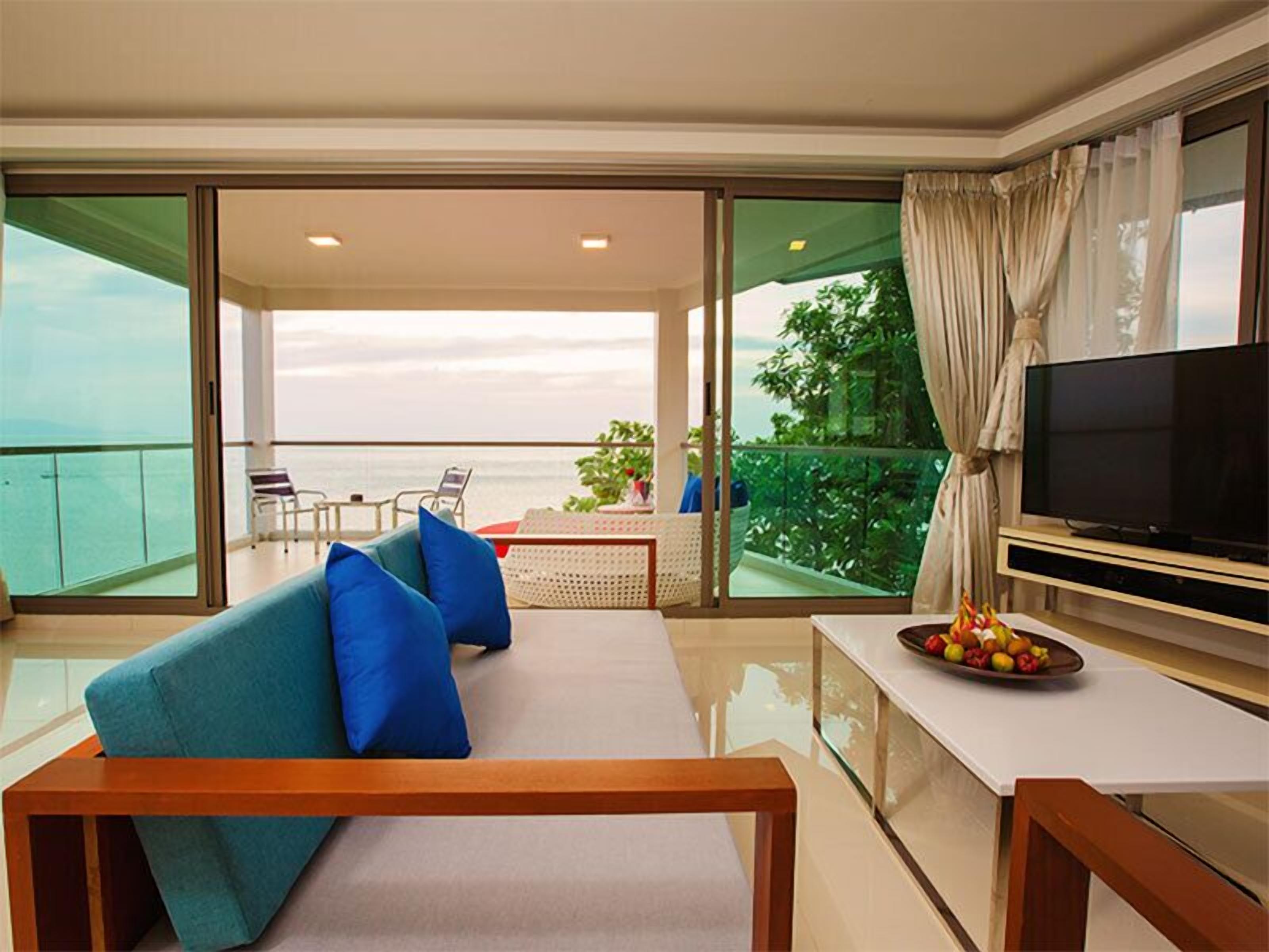A balcony with a sofa, a dining table with fruit, and a TV.
