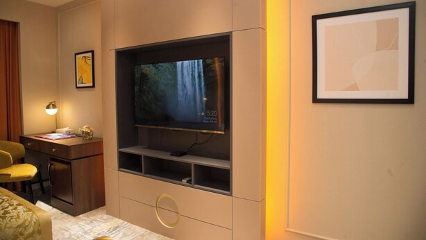 A modern living room with a flat-screen TV mounted on a wall, a desk with a lamp, a chair, and a sofa. - Bayangol Hotel (Ulaanbaatar)