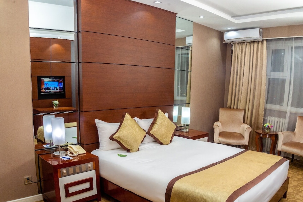 A hotel room with a large bed, a TV mounted on the wall, a desk with a telephone, and a chair.